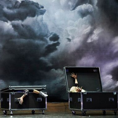 Zwei Flyht Cases mit Rollen, die wie Särge nebeneinander auf der Bühne stehen. Die linke Box ist fast zugeklappt, ein Arm und ein Bein ragen heraus. Die rechte Kiste ist aufgeklappt und ein Vampir, der in der Kiste liegt, streckt seine Arme zu beiden Seiten aus. Im Hintergrund ist ein Himmel mit dunklen Wolken zu sehen.