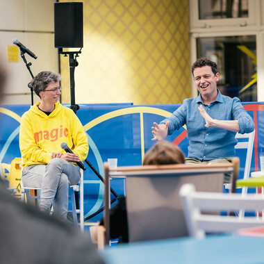 Anna Mülter and Richard Dougherty in conversation. They are sitting in the festival centre. Richard bends BSL, Anna looks at him attentively.