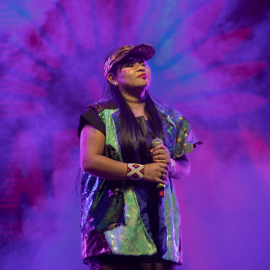 Anarandá MC on stage. Anarandá wears a cap on her head and holds a microphone in her hand. Her eyes are closed. She is wearing a loose-fitting T-shirt.