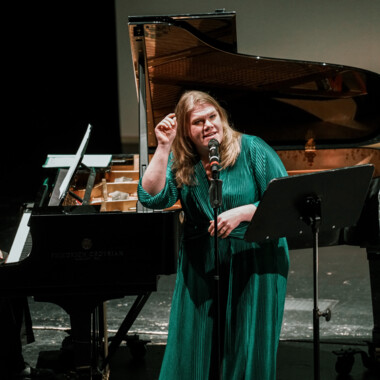 Gisa Flake in a green dress standing in front of a microphone.
