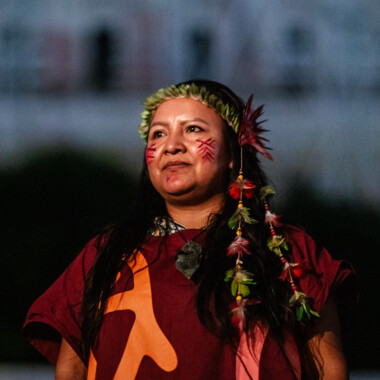 One person of the Baniwa community, her face is painted, she wears a headdress made of beads and plants.
