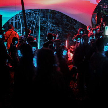 Viele Personen mit blau leuchtenden Kopfhörern tanzend im Festivalzentrum.