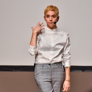Diana Anselmo steht hell gekleidet vor einer weißen Wand und performt.
