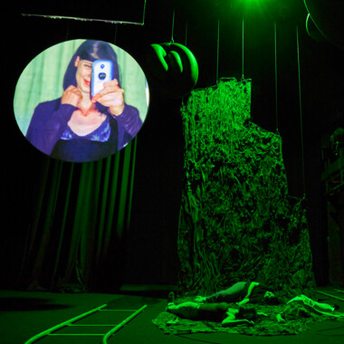 Three people are lying on the floor, a round projection screen hangs from the ceiling, showing a person holding a phone in front of their face.