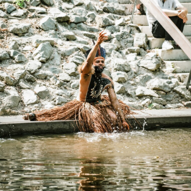 Ein Performer in traditioneller Kleidung spritzt während einer Aufführung Wasser in die Luft.