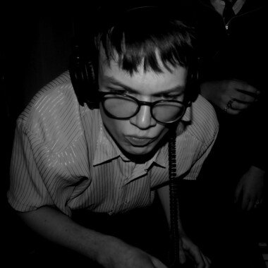 Schwarz-Weiß-Aufnahme von einem DJ mit Brille und Kopfhörern, der sich nach vorne beugt. 