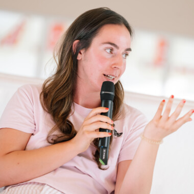 A person speaks into a microphone and gestures with her other hand.