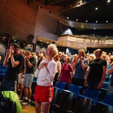 Das Publikum steht im Theater und hält sich zum Teil die Ohren zu.