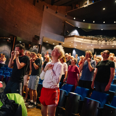 The audience stands in the theatre, some of them covering their ears.