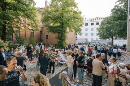 Viele Menschen im Festivalzentrum im Theaterhof. In kleinen Gruppen stehen oder sitzen sie beisammen, unterhalten sich, manche trinken Sekt.