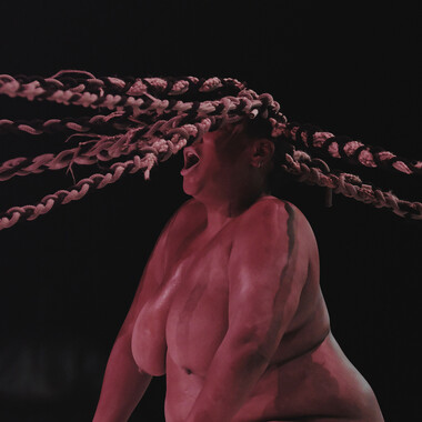 Image description by the editorial staff of Festival Theaterformen. Self-description of the depicted persons follows. / A nude person from the waist up with her mouth open is swinging her long, braided hair in a circle.