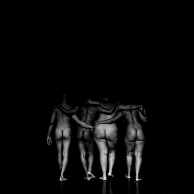 Image description by the editorial staff of Festival Theaterformen. Self-description of the depicted persons follows. / A black and white photo of four nude performers from the back in front of a black background. They are holding each other by their shoulders and hips and are walking towards the background, facing away from the audience. 