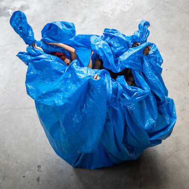 People wrap themselves with a large canvas. Arms and heads of some stick out from the top.