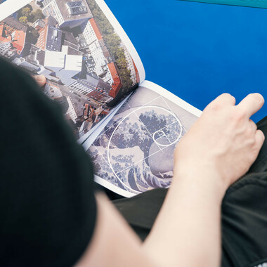 A person is leafing through an illustrated book. On the left side of the volume is the Schauspielhaus Hannover, on the right side the drawing of a wave, from which the abstract floor covering of the festival centre is derived.