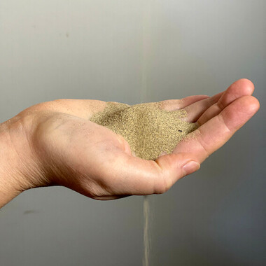 Nahaufnahme einer Hand, in die Sand hinein rieselt.