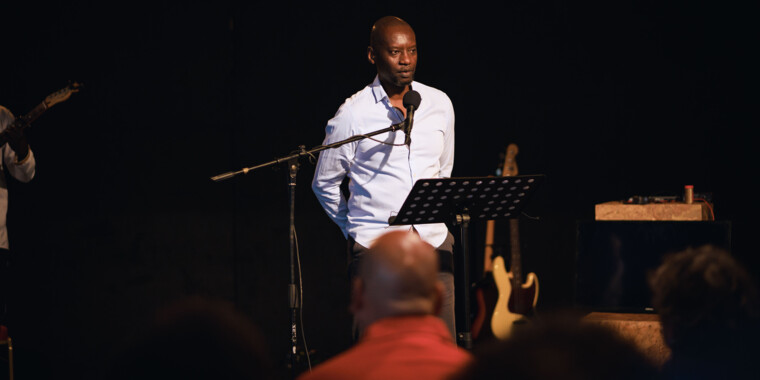 Dorcy Rugamba speaks into a microphone, a music stand in front of him.