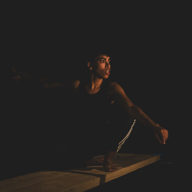 Bühnensituation: Eman Hussein sitzt auf einem Holzbrett und schaut ins Licht.